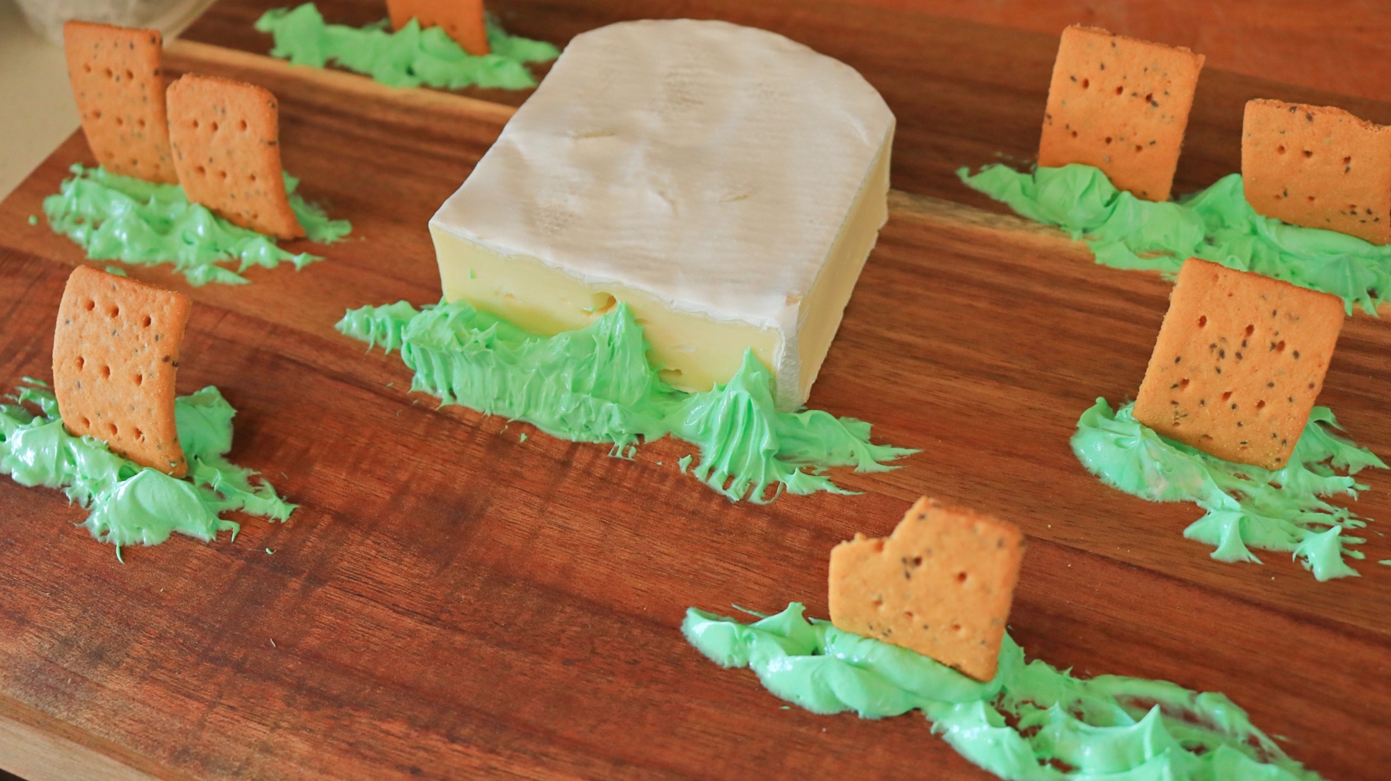 Green dyed cream cheese and crackers on a cutting board.