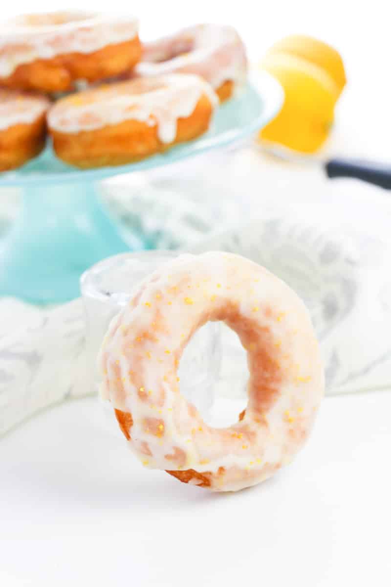 glazed donut leaning on clear glass with stacked donuts in background